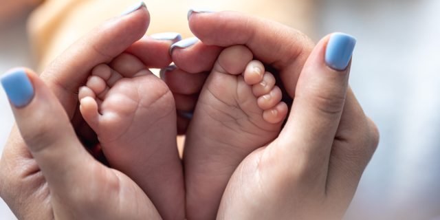 mom holds the legs of a newborn baby in her hands.